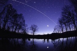 A Discovery űrsikló és a Nemzetközi Űrállomás íve Bakonybélben a Borostyán-kút tavacskája felett a szürkület színeiben. Alattuk a Hold és a Jupiter fénye tükröződik a víz felszínén.